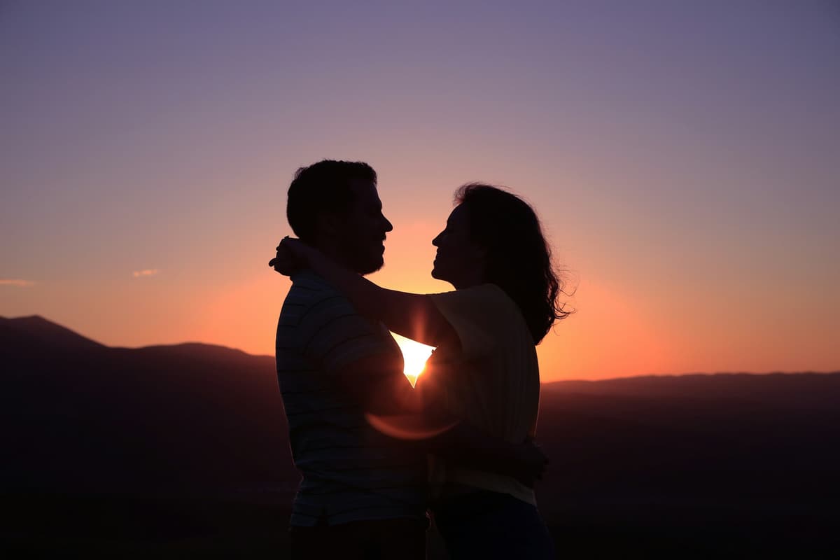 Couple making a heart shape with their hands at sunset